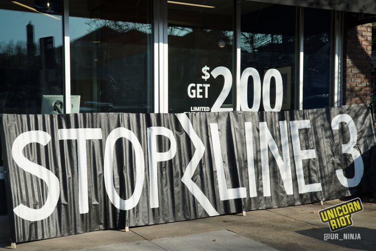 large black banner reading "Stop Line 3" in white, placed alongside front of brand-new Chase Bank branch in St. Paul, MN.