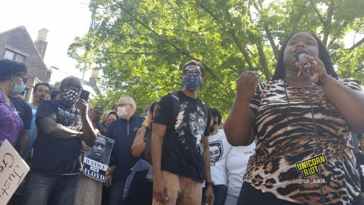 Governor Tim Walz and his spose Gwen listen as Nekima Levy Armstrong speaks at a Justice For Floyd 'Jail Killer Cops' event in Saint Paul, Minnesota. The protest took place outside the governor's residence. Walz is standing beside a protester holding a "Justice For Floyd" sign.
