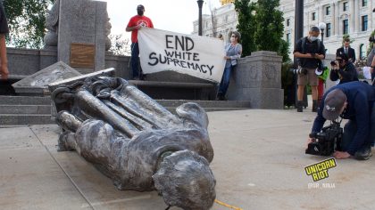 Statue of Columbus laying on the ground with sign saying End White Supremacy in background