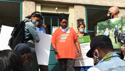 image: a Black woman in an orange shirt is adding tape to a piece of paper, a list of demands for the Minneapolis Parks & Recreation Board Superintendent, Al Bangoura. On the woman's left is a Lakota man with chest-length black hair, as well as a media-maker with their back turned. On the right is a member of Minneapolis Parks & Power; he is wearing a mask and holding a blown-up photograph from when Minneapolis Police assisted in the violent clearing of the sanctuary encampment at Powderhorn Park on Friday, August 14, 2020.