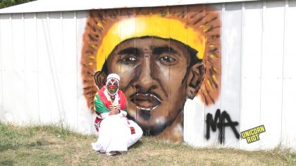 Oromo woman kneels next to mural of Hanchalu Hundessa on the back of the Minnesota Oromo Community Center
