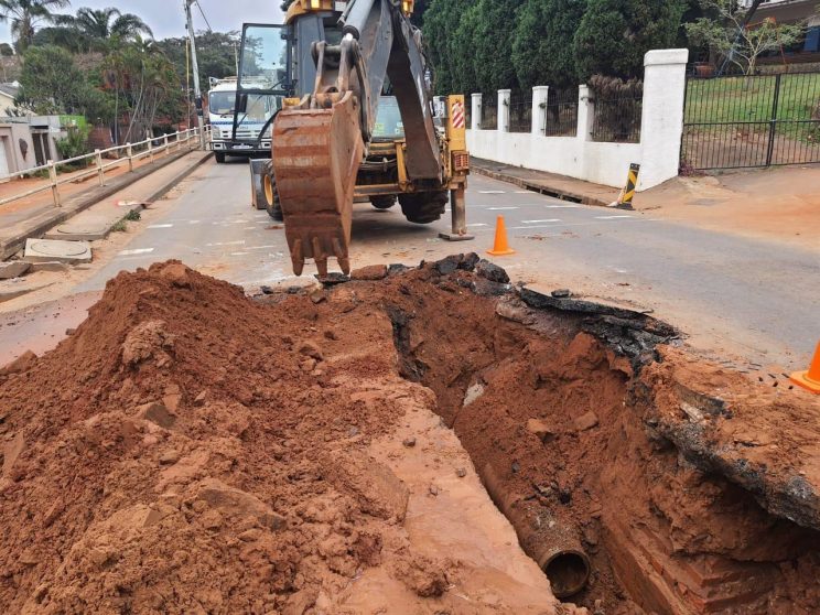 Excavator digs around water pipe on road