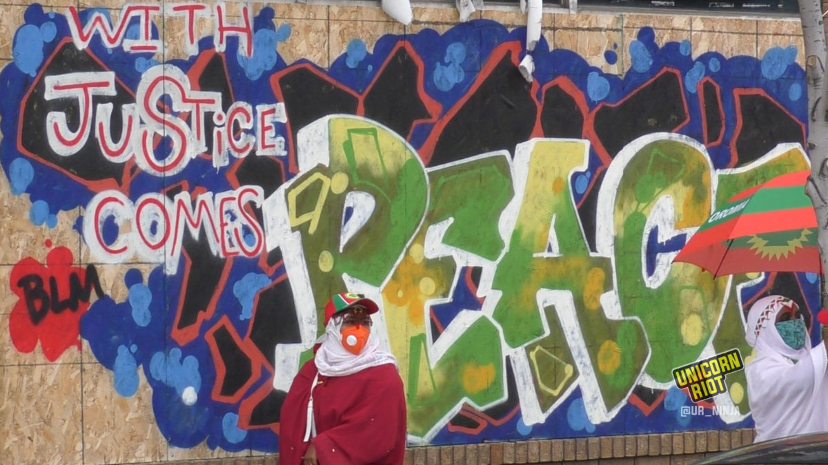 Oromo women stand in front of BLM mural saying "With Justice Comes Peace"