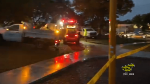 image: city emergency vehicle lights, as well as other city vehicles' lights, shine in the pre-dawn twilight light as well as reflect off the wet sidewalks at Peavey Park. Yellow caution tape has been strung up around the park as a barrier while police evict the residents from more than 10 tents.