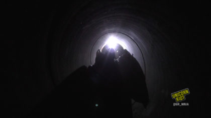 Three people inside a dark pipeline slightly illuminated by a headlamp