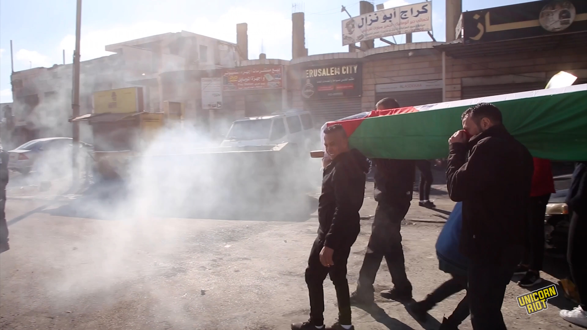 Palestinian protesters carrying a mock-coffin brace as tear gas visibly enters their space