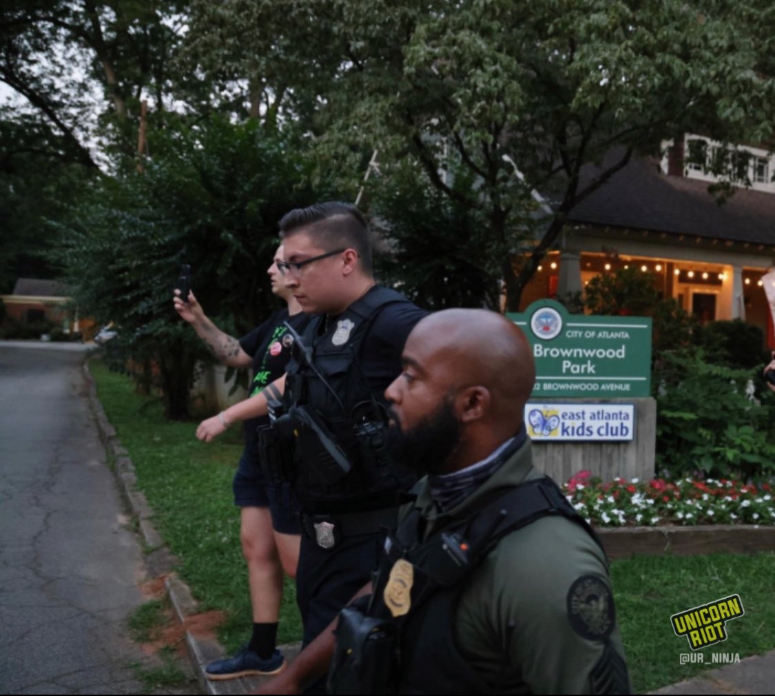 Two Atlanta Police officers in tactical vests walk past the entrance sign to Brownwood Park that also reads “east Atlanta kids club” after sweeping through the park as the vigil for Manuel ‘Tortuguita’ Terán was set to begin at 8:30 p.m.