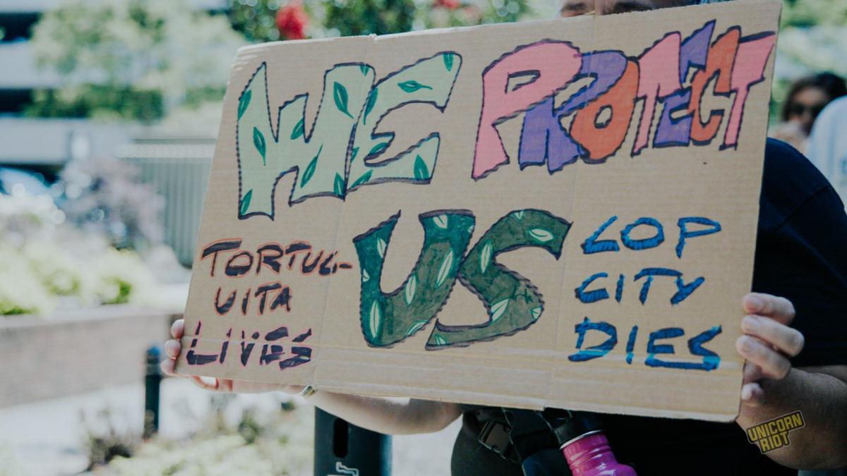 A cardboard protest sign reads "We Protect Us - Tortuguita Lives - Cop City Dies"