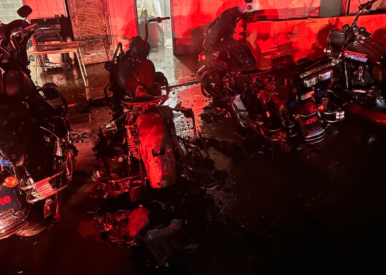 Crime scene photo showing burnt-out Atlanta Police motorcycles in a parking lot at the Atlanta Police Training Academy. The image is washed in a red light presumably from a police or fire department vehicle from out-of-frame.