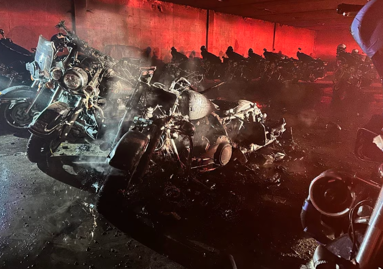 Crime scene photo showing burnt-out Atlanta Police motorcycles in a parking lot at the Atlanta Police Training Academy. The image is washed in a red light presumably from a police or fire department vehicle from out-of-frame.